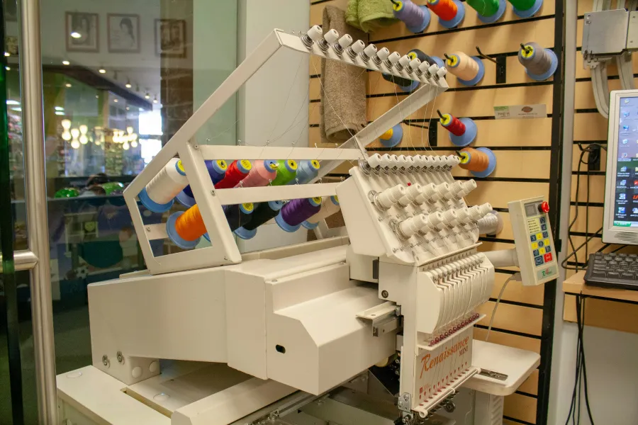 Industrial embroidery machine surrounded by colorful thread cones in a working studio